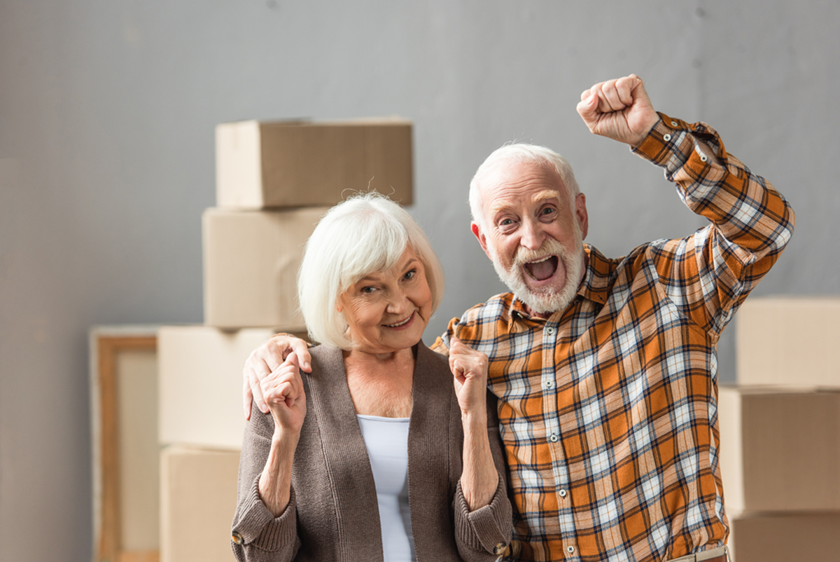 Happy Retired Couple With Moving Boxes Behind Them